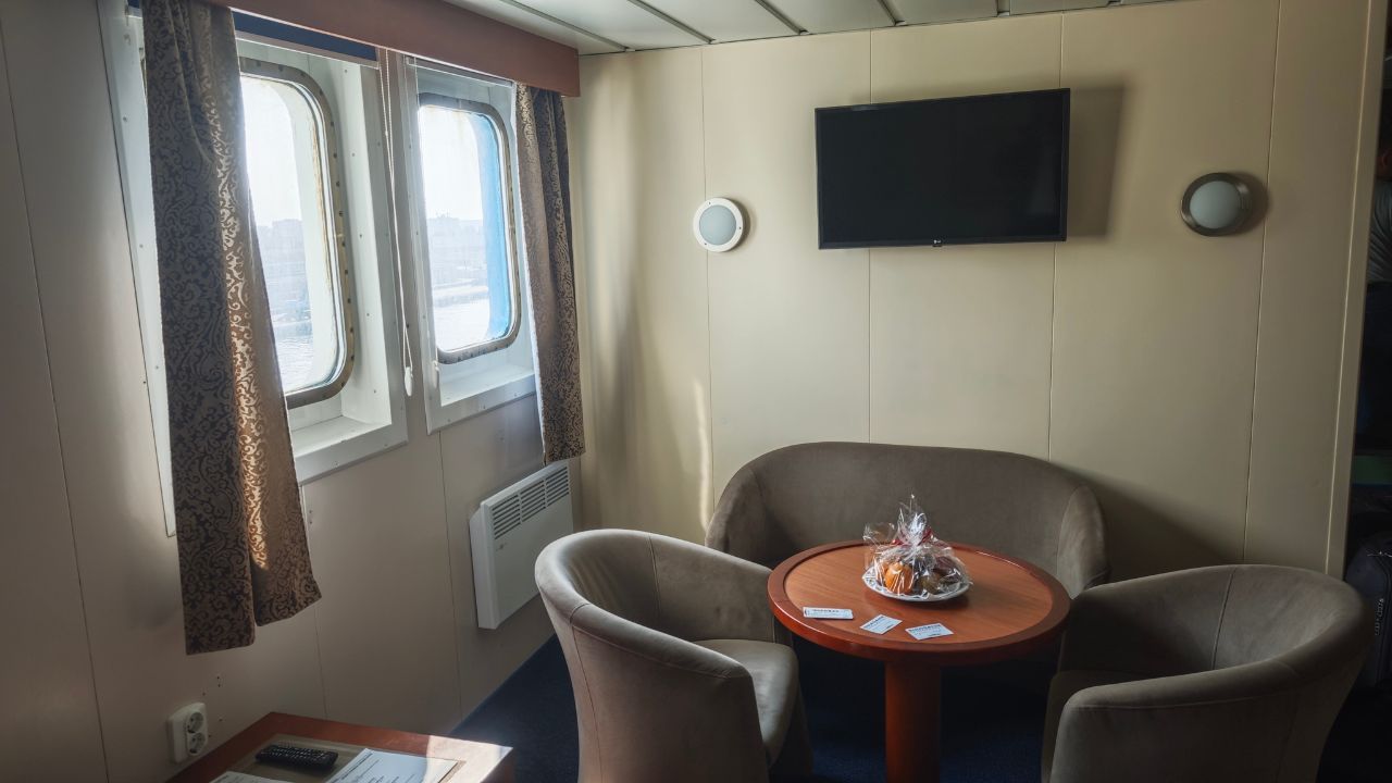 Gdansk, Poland - 06.05.2025: Cozy ferry cabin interior with two windows, round table, armchairs and a TV on the wall, daylight streaming in