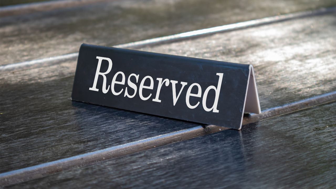 Reserved sign, reservation concept. Text reserved on metal black color plate, white color letters, on wooden table. Close up view with details