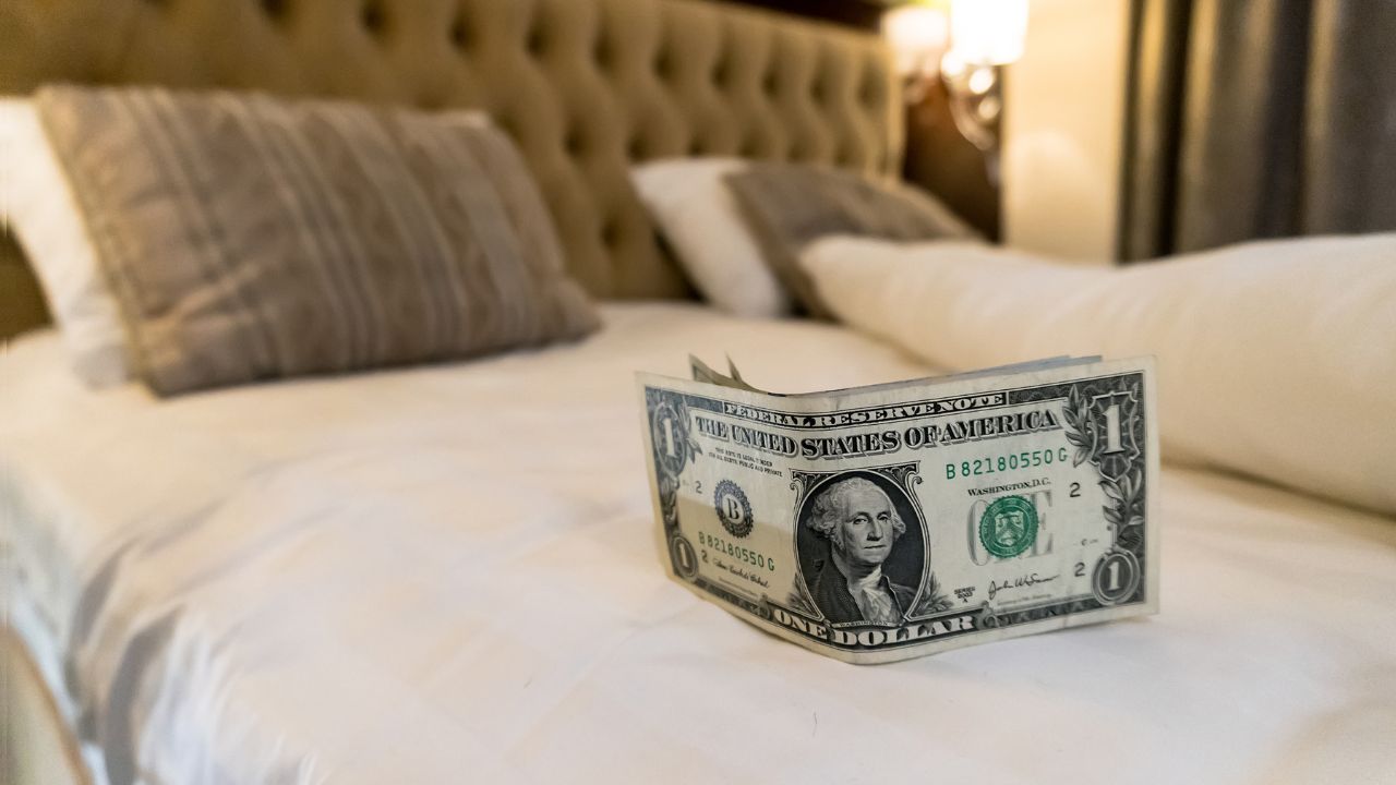 paying us money dollar on white bed in hotel. tips left on the bed for the maid of the hotel room. Tips at the bed for the housekeeper in hotel room.