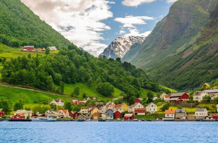 A lots of little colorful traditional Norwegian houses near the sea with green forest on mountains on background and blue sky with dark clouds, Sognefjord, Norway