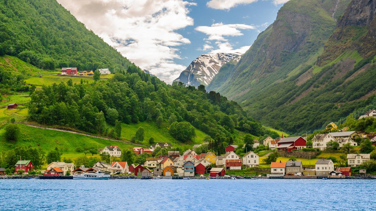 A lots of little colorful traditional Norwegian houses near the sea with green forest on mountains on background and blue sky with dark clouds, Sognefjord, Norway