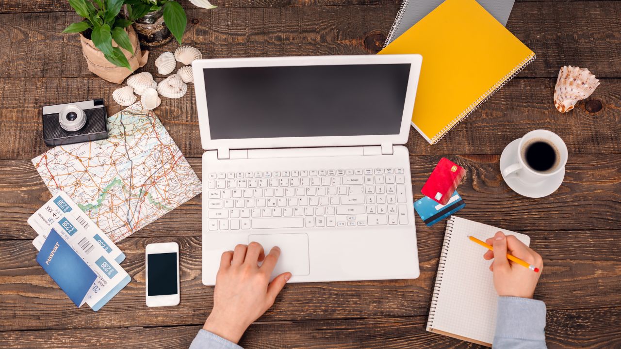 Top view creative photo of objects and hands on vintage brown wooden table. There are map, tickets, credit cards, coffee, laptop and mobile phone on it