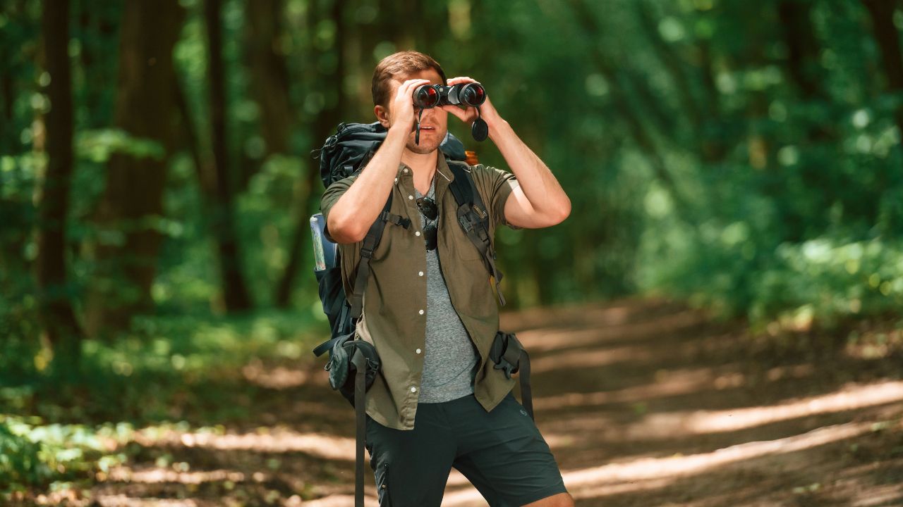 Looking through the binoculars. Tourist in summer forest. Conception of exploration and leisure.