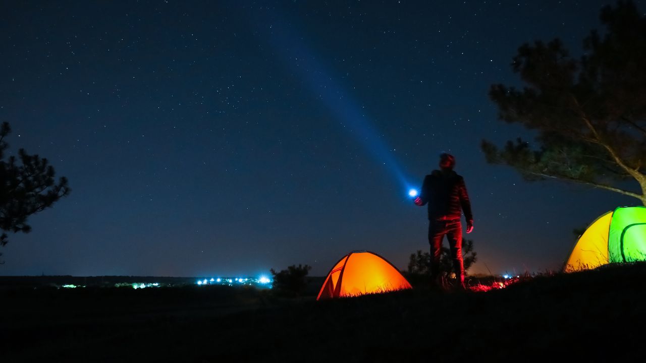 Camper with flashlight near tents at night