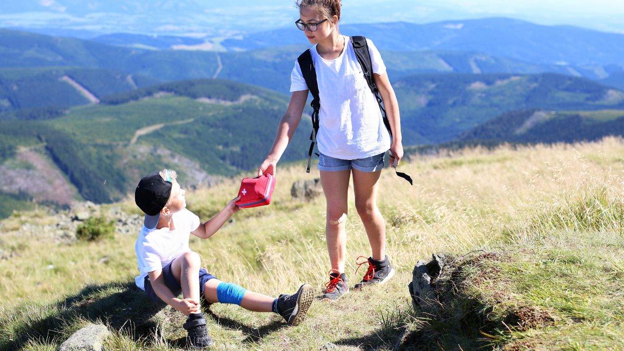 Child handing a first aid kit to another hiker in the mountains