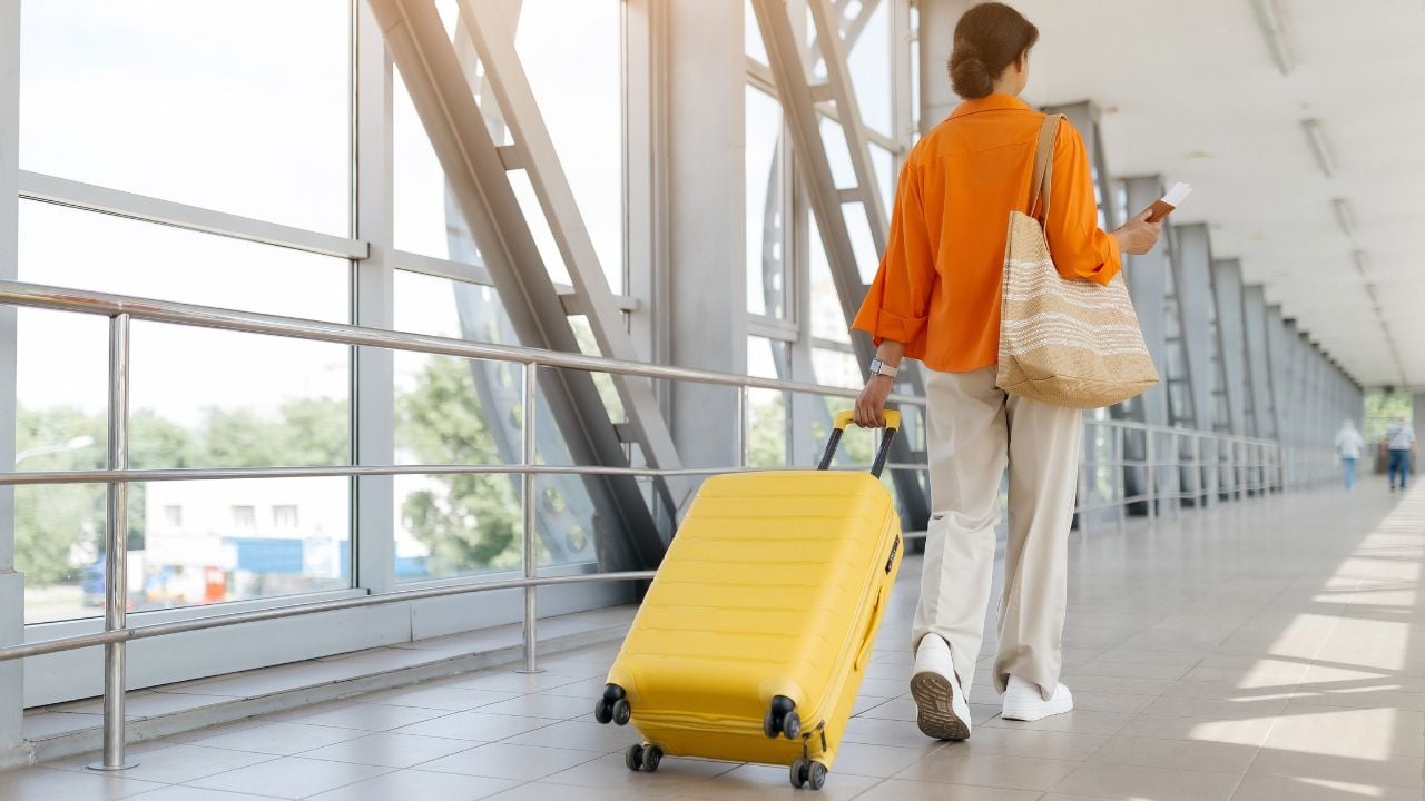 Rear view of black traveler woman walking through airport terminal with suitcase