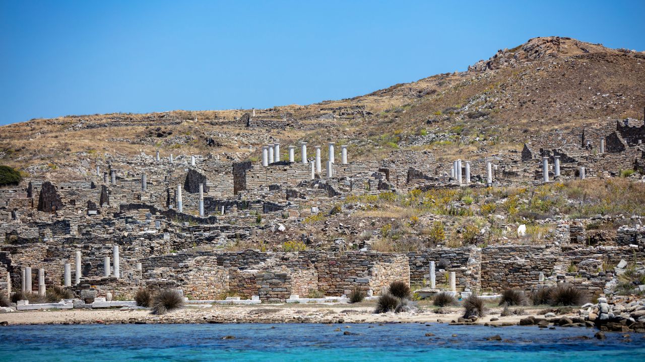 Delos in the Cyclades, seen from a boat with ruins and marble columns on a rocky hillside