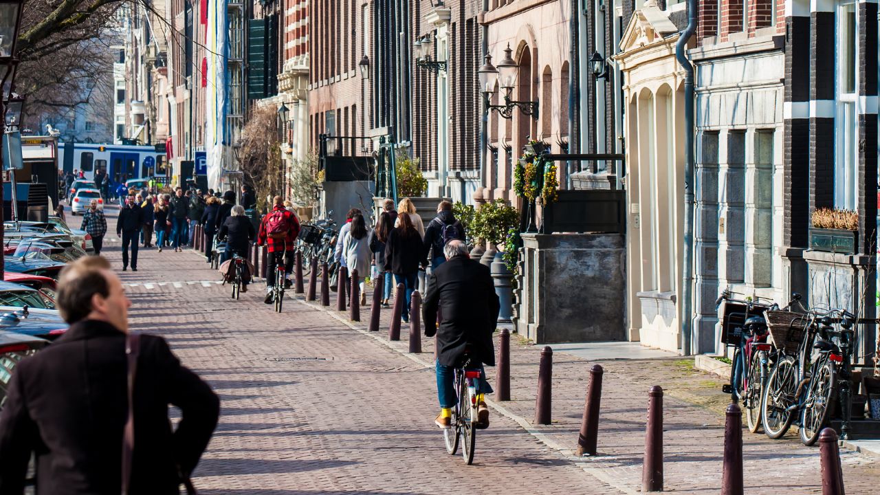 AMSTERDAM, NETHERLANDS - MARCH, 2018: People walking and riding bicycles at the beautiful cobblestone streets next to the canals of the Old Central district of Amsterdam