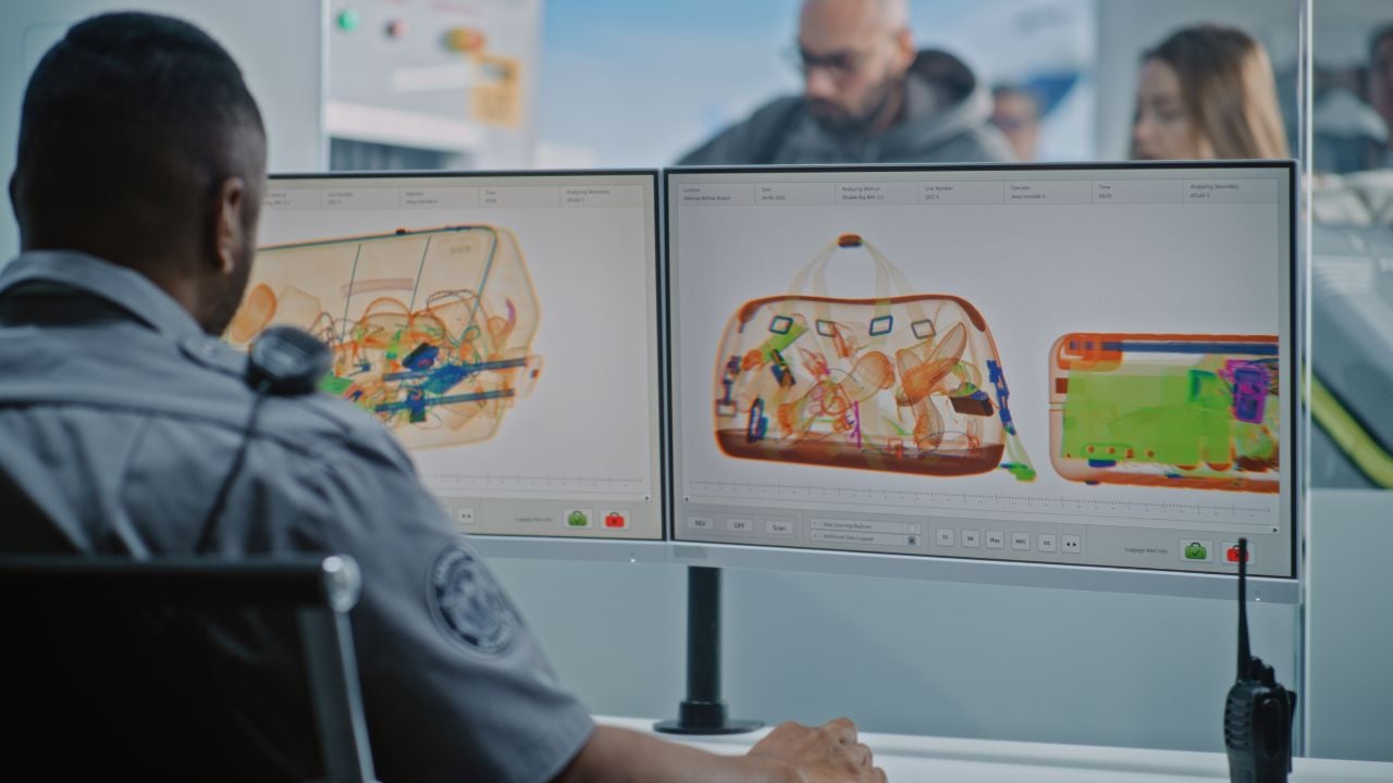 Airport Security Checkpoint: African American Security Officer Monitoring X-ray Scanning of Luggage on Computer Screens Using Software. Diverse People with Carry-On Baggage During Screening Procedure.