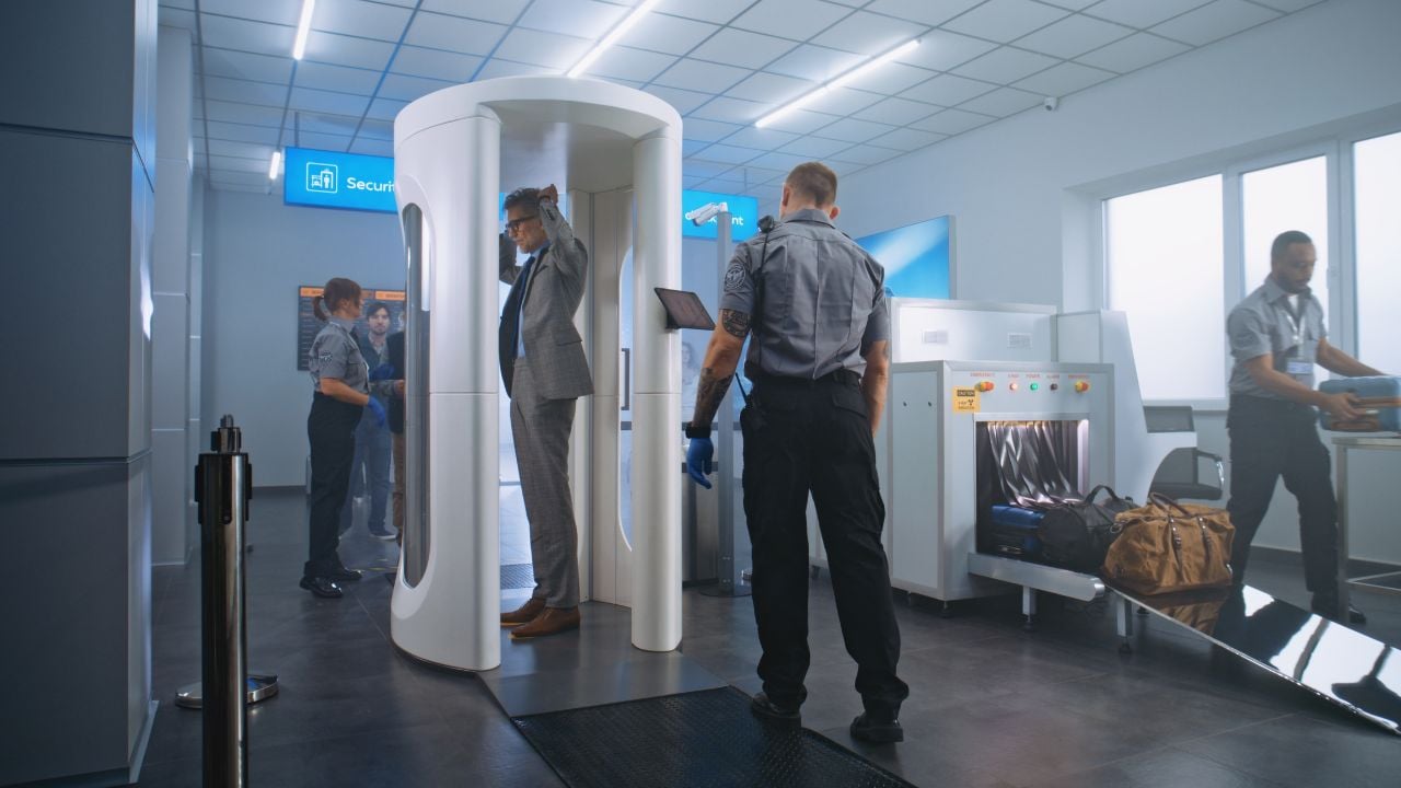 Airport Terminal Checkpoint: Diverse People Walking Through Metal Detector Gates, Taking Luggage from Conveyor Belt. Security Officers Control Scanning of Passengers. Group of Tourists Going on Trips.