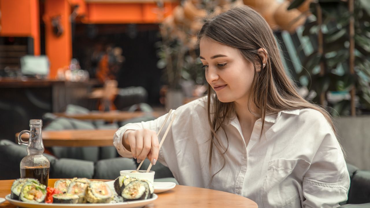 Young Woman eating and enjoying fresh sushi in luxury restaurant. Female client holding food sticks and eating oriental meal on lunch. Concept of food.