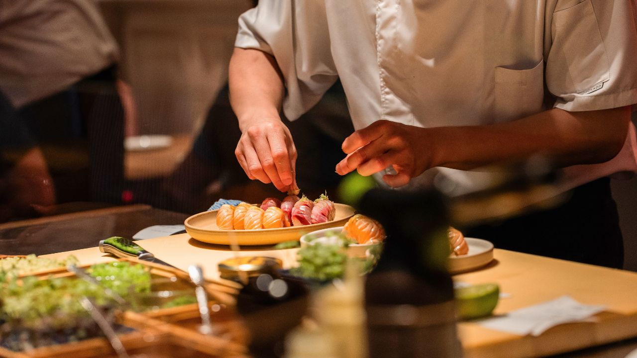 Sushi chef skillfully prepares fresh sushi rolls, showcasing vibrant ingredients and meticulous technique in a lively culinary environment.