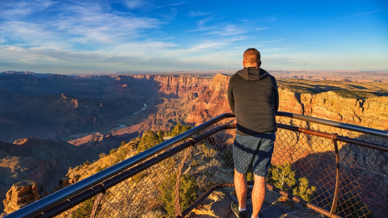Tourist Viewing Grand Canyon from Navajo Point Overlook during golden hour, featuring vibrant canyon walls and the Colorado River winding through the landscape.