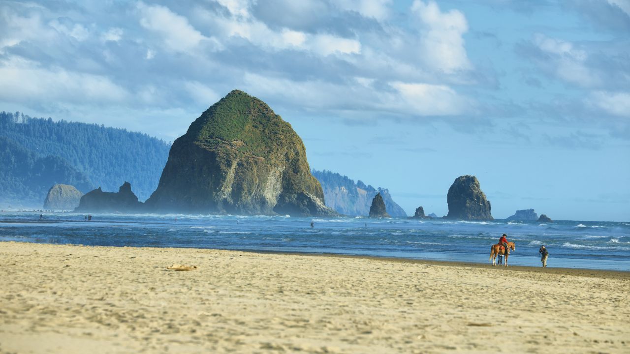 CANNON BEACH, USA - JUNE 18, 2016: horseman and other unidentified people in Cannon Beach with Haystack Rock in the background, Oregon, USA