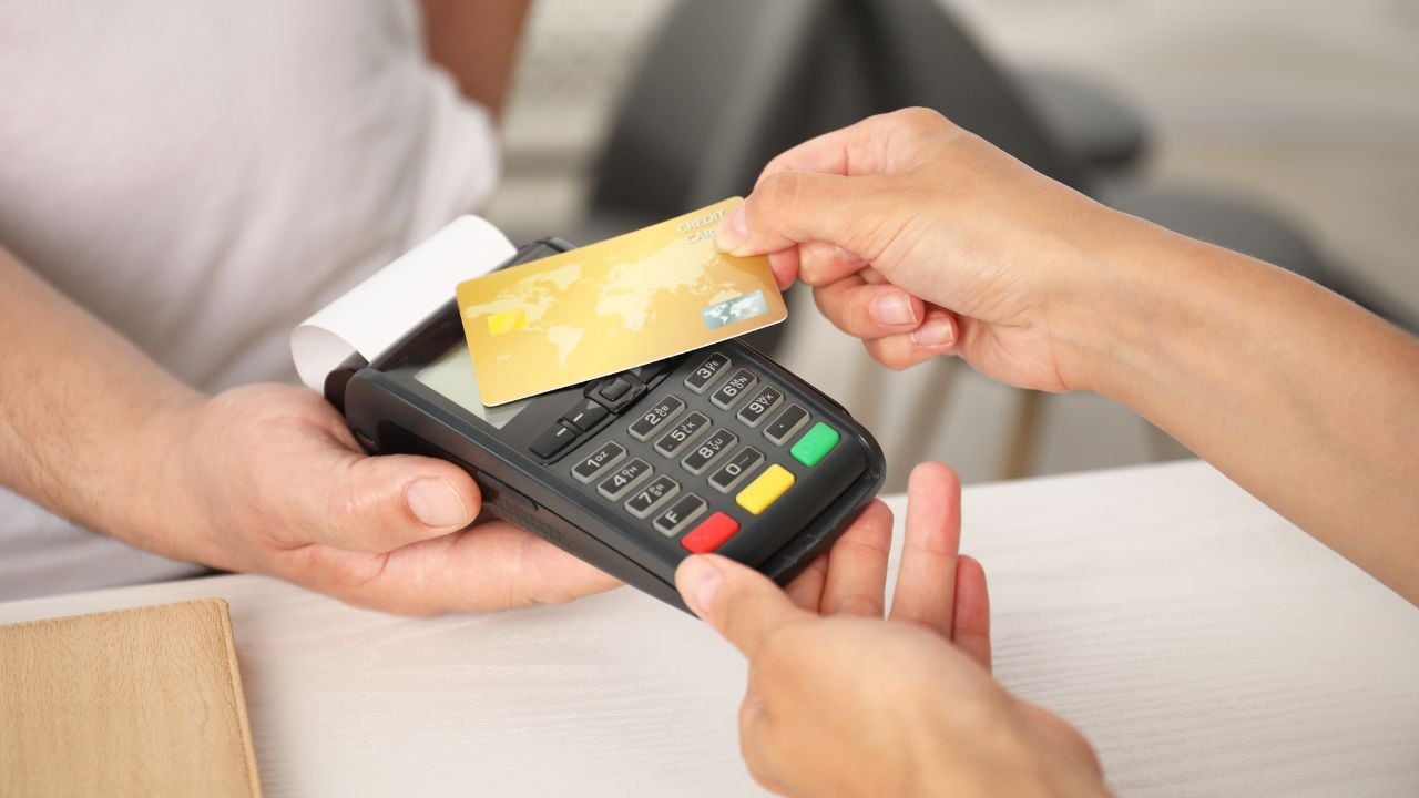 Man taking payment from client via credit card terminal at white wooden table, closeup