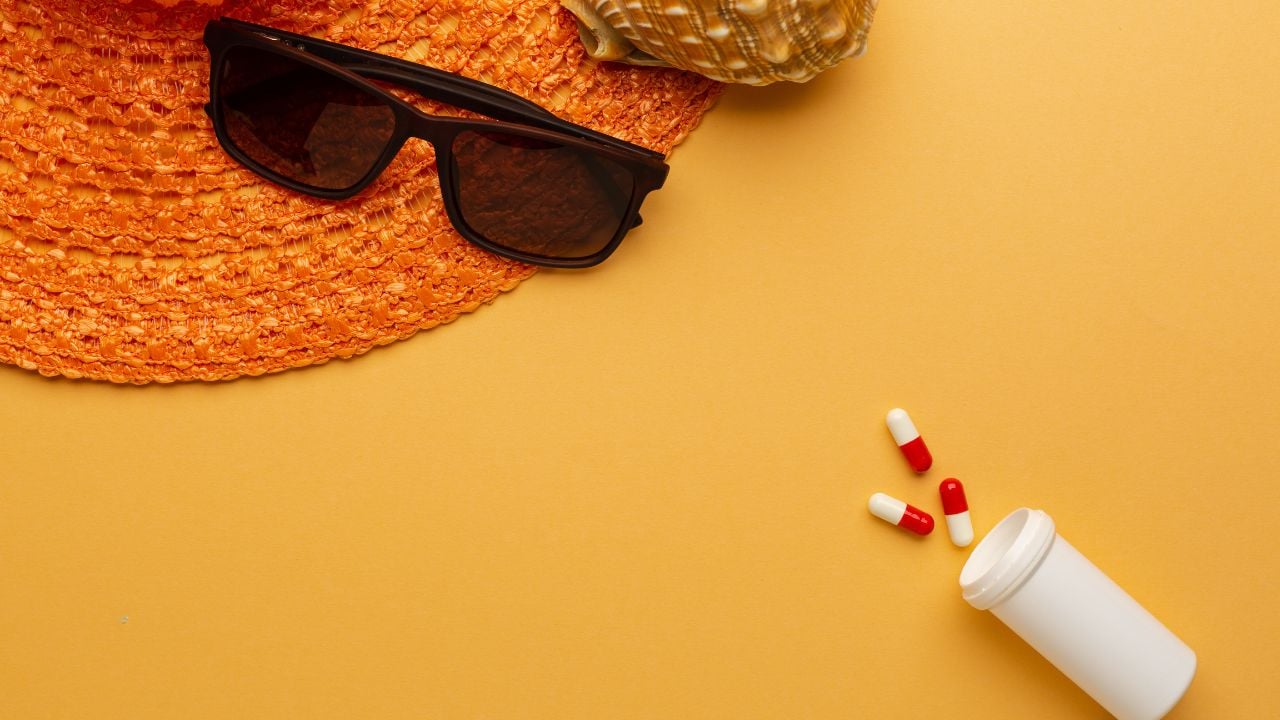 Sunglasses and hat with pills on orange background as a concept of vacation with protection on pandemic situation.