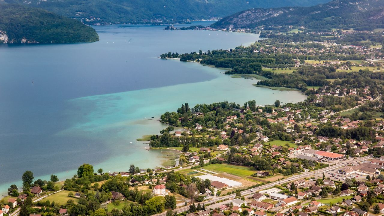 View of the Annecy lake surrounded of mountains with cityscape in cloudy weather. Rhone Alps, France.