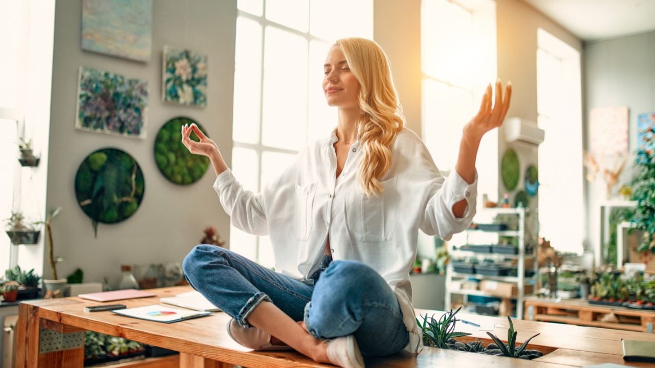 Keep calm and no stress! Young woman is sitting in lotus position in office. Taking pause during hard work and relaxing