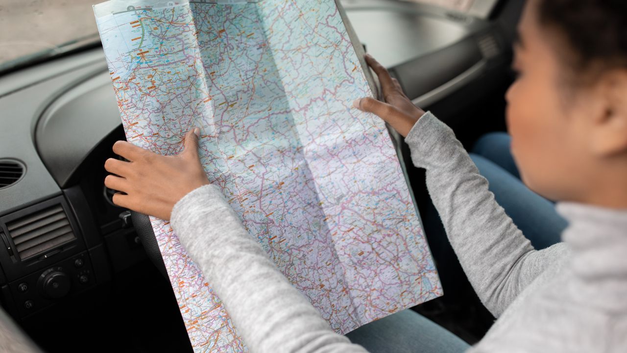 Using map in road trip for directions in new city at travel. Young serious attractive african american woman reading chart while sitting in car, planning route and exploring way, empty space, cropped