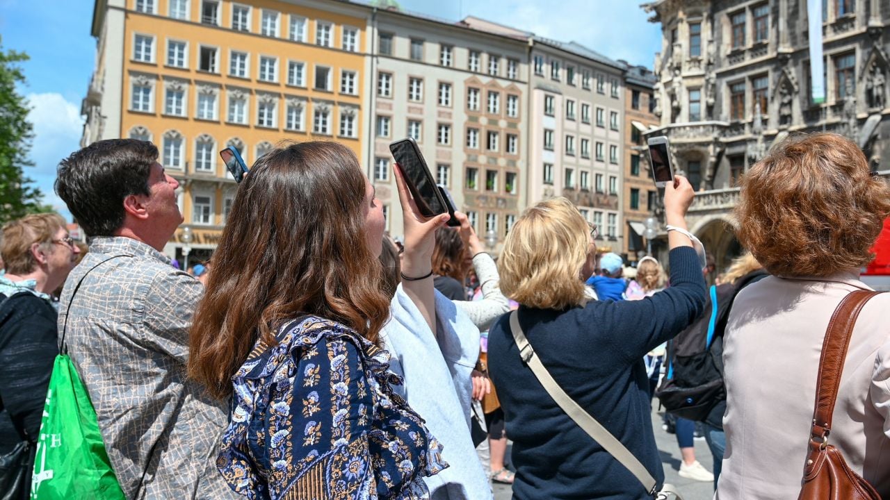 Munich, Germany, May 2022: People taking photos with smartphones in city centre. Tourists with mobile phones in their hands.