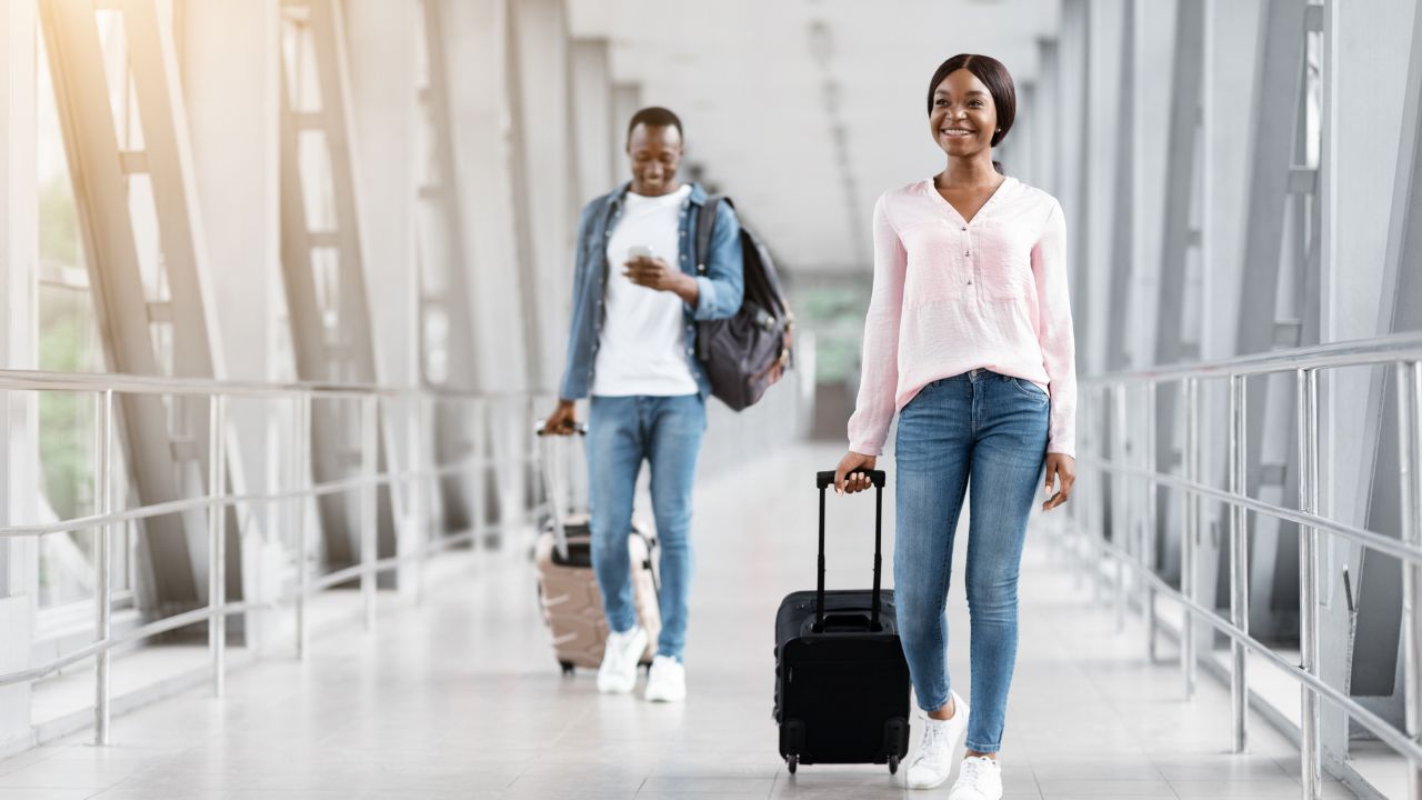 Portrait Of Young Black Travellers Walking In Airport Terminal With Suitcases, Happy African American Man And Woman Carrying Luggage Going To Departure Gate, Ready For Vacation Travel, Free Space