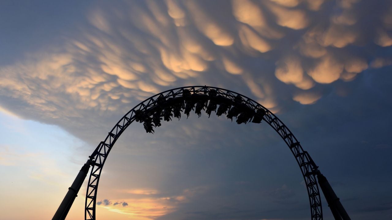 Silhouette of people having fun on a roller-coaster in an amusement park at sunset. Adrenalin concept.