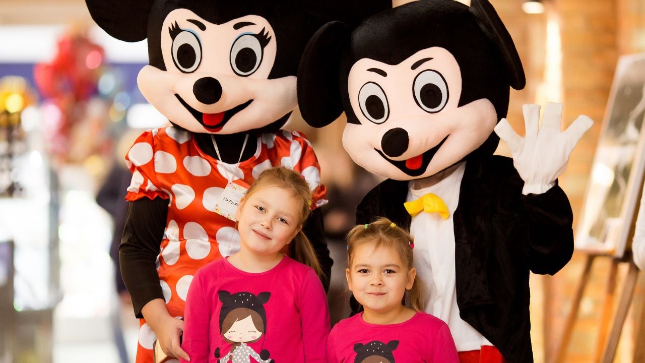 Two adorable girl with mickey and minnie mouse posing in shopping center, smiling and having fun in New York, USA in 2018