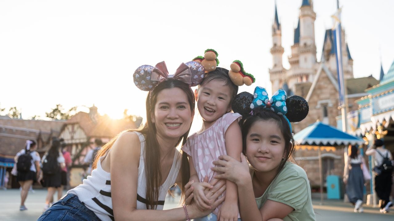 Portrait of Asian mother and two daughter traveling in the theme park. Happy family, attractive woman and children feel happy and relax, spend time for vacation at amusement park and look at camera.