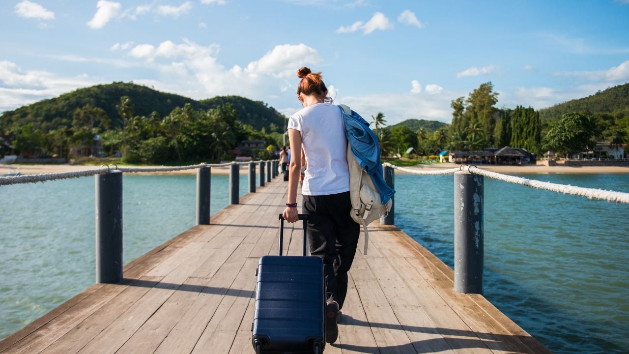 Girl tourist dragging luggage on a dock to tropical beachGirl tourist dragging luggage on a dock to tropical beach