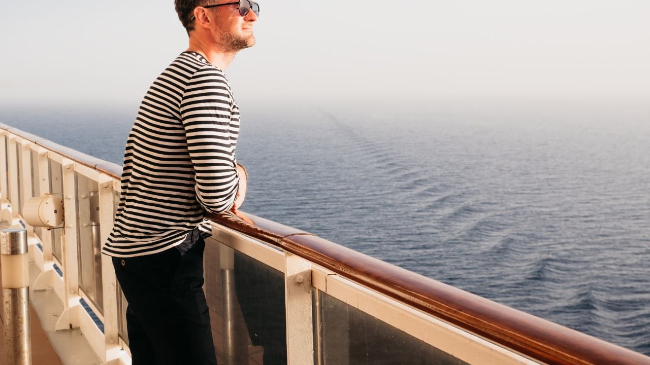 Handsome man standing on the empty deck of a cruise ship. Sunny morning, clear day. Closeup, outdoor. Vacation and travel concept