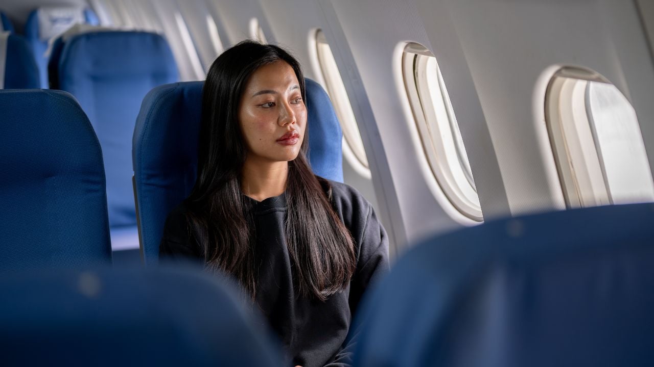 A thoughtful, lonely Asian woman in a cozy black sweater travels alone on holiday, sitting on the flight with a sad expression, gazing out the window. people, transport, lifestyle