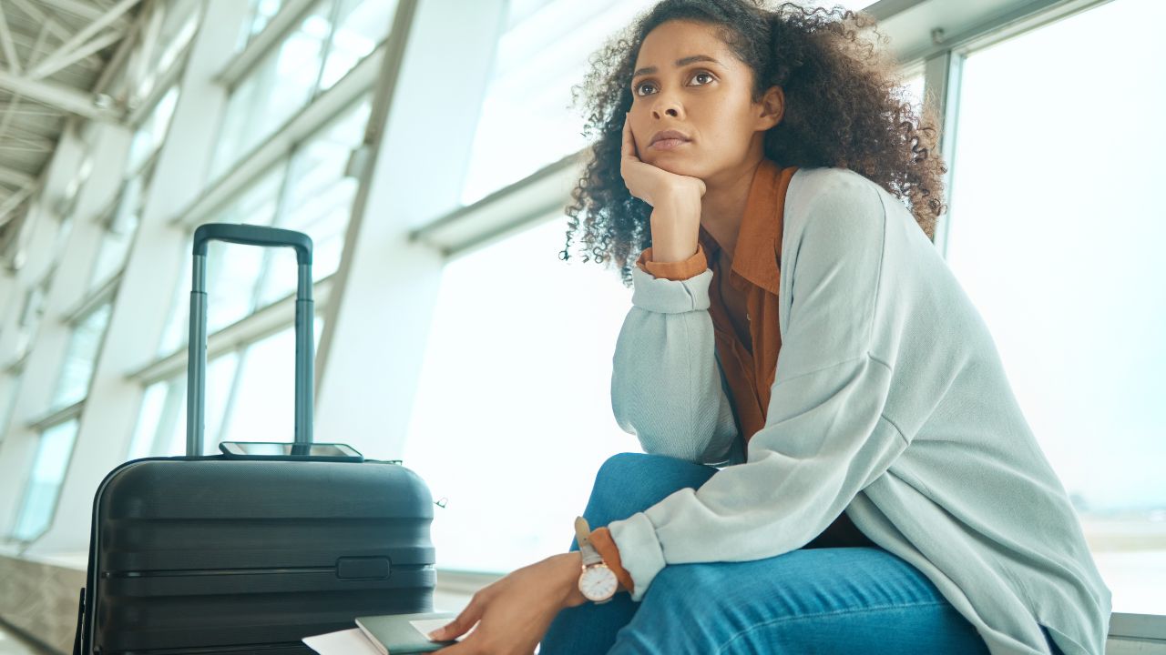 Airport, travel delay and sad woman with anxiety for immigration, passport problem or schedule. Young USA person with luggage and stress, worry or thinking of flight fail, crisis or identity mistake