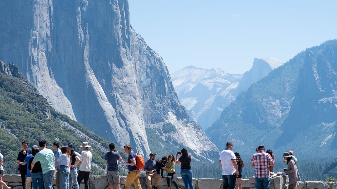 A group of visitors stands at the stone railing of Tunnel View, admiring the sweeping vista of Yosemite Valley and El Capitan, Yosemite, CA, July 21, 2019