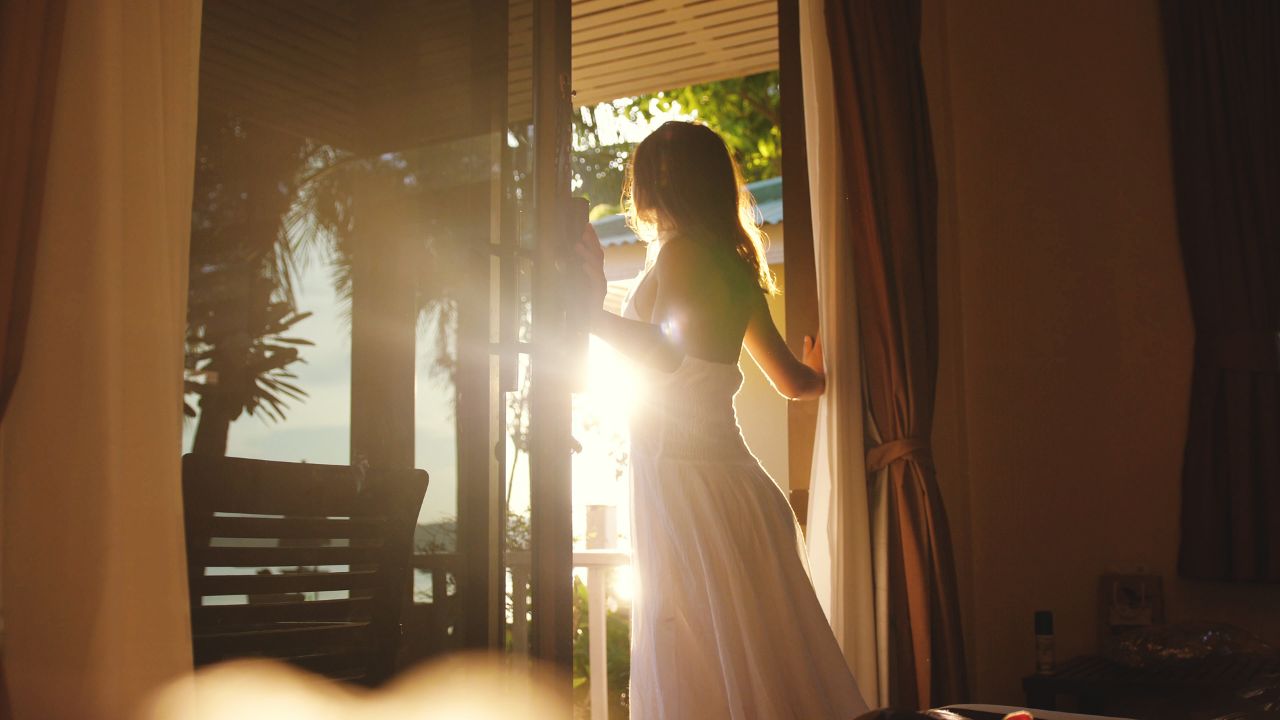 Brunette girl opens the door in the early morning during sunrise with lens flare effects