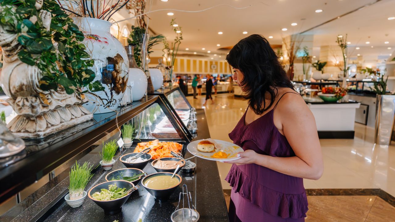 Kemer, Tureky - september 18, 2025 - Woman in a purple dress selecting food from a buffet at a hotel restaurant. She holds a plate with food while choosing among sauces, salads, and appetizers.