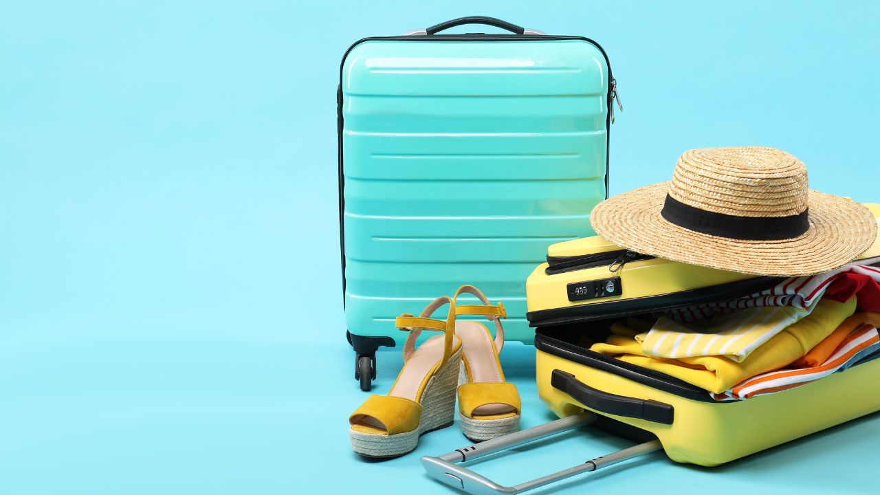 Suitcases with clothes, shoes and wicker hat on light blue background