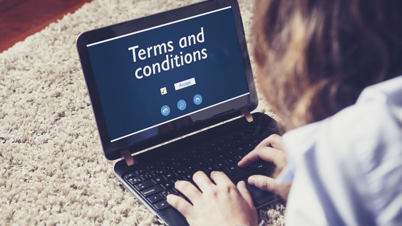 Woman reading Terms and conditions on line with a laptop, lying on the floor at home.