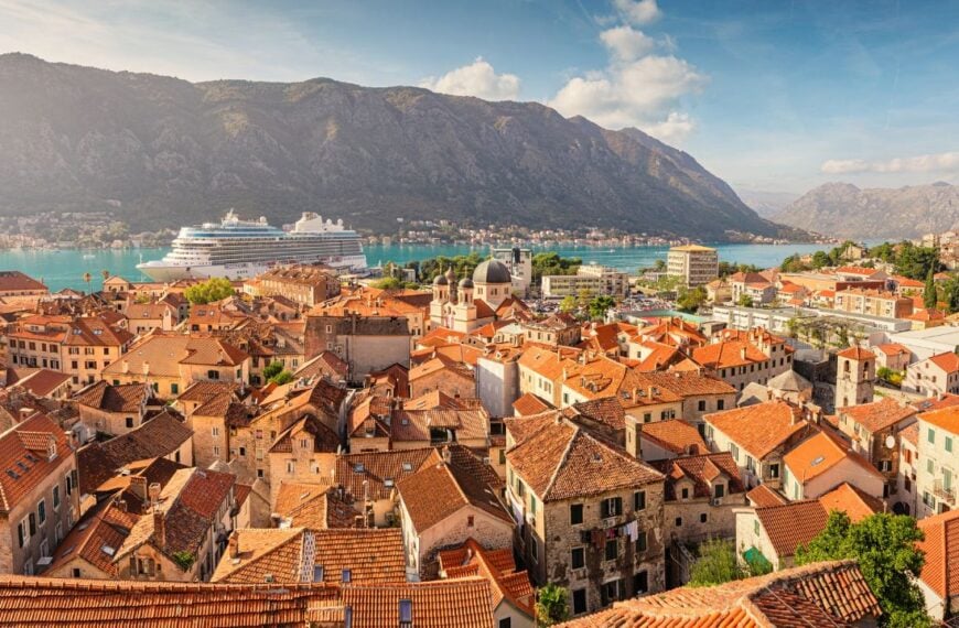Panoramic view of Kotor old town with its orange roofs, a cruise ship docking in the bay, and the surrounding mountains creating a stunning backdrop of Montenegro