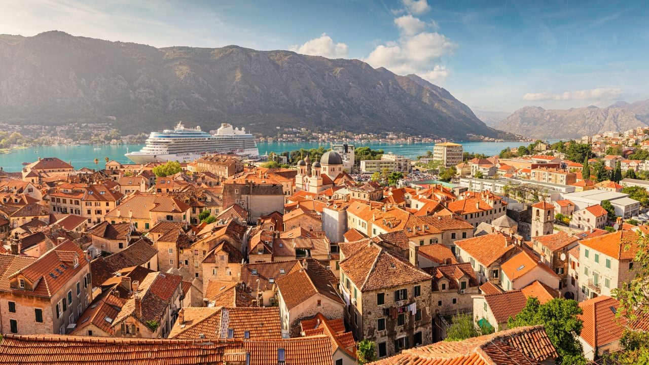 Panoramic view of Kotor old town with its orange roofs, a cruise ship docking in the bay, and the surrounding mountains creating a stunning backdrop of Montenegro