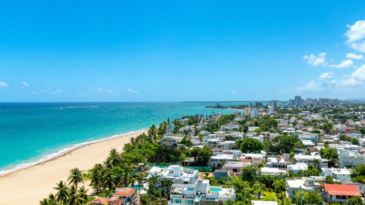 Aerial view of Ocean Park in San Juan, Puerto Rico, showcasing the wide sandy beach, turquoise ocean, and residential areas filled with homes, and the Caribbean ocean skyline in the background.