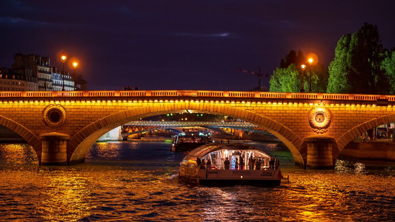 Paris, France, August 19,2018:Bateau Mouche cruising on Seine river at sunset, Paris. Beautifully lit old bridge at Seine river at dusk.
