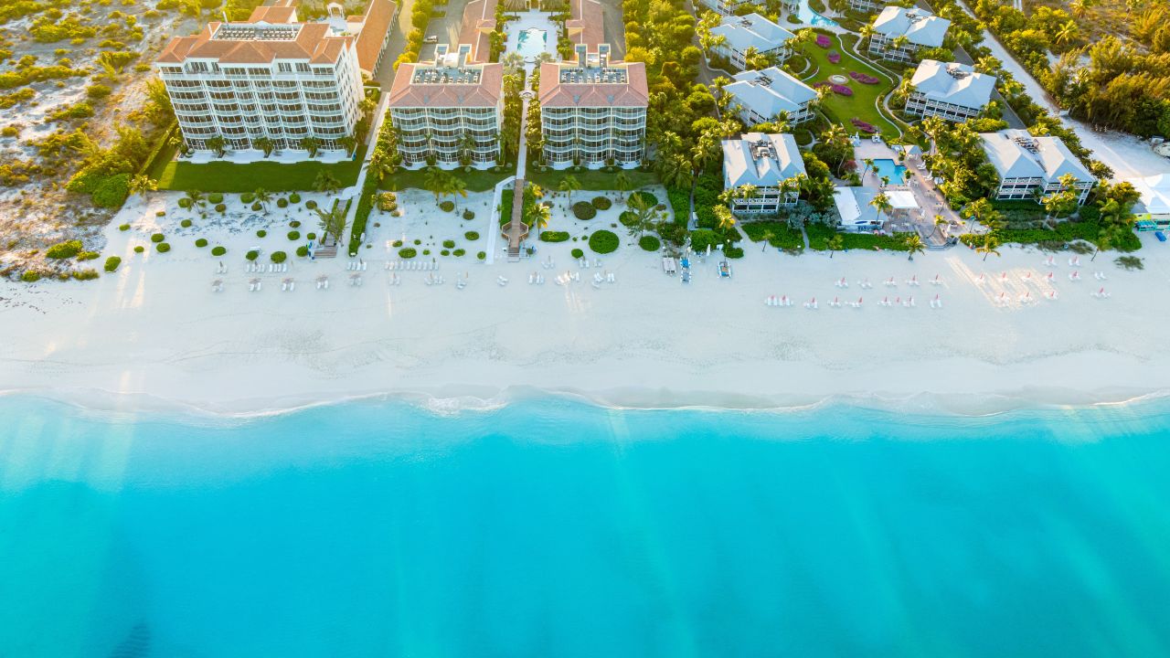 Grace Bay, Turks and Caicos - February 20 2021: Golden sunrise bursts over a stretch of land and resorts along Grace Bay Beach with its white sandy shore and blue waves in foreground