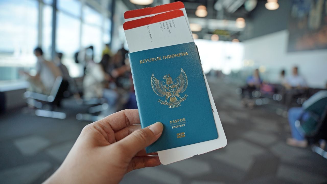 Close-up photo of man's hand holding passport with flight ticket or boarding pass at airport