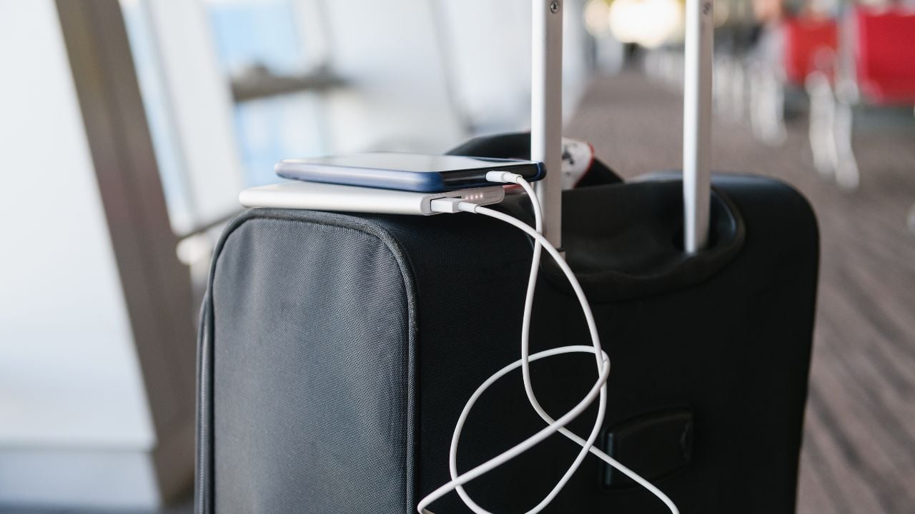 Cellphone recharge with portable charger by usb cable on black travel bag luggage handle at airport close up