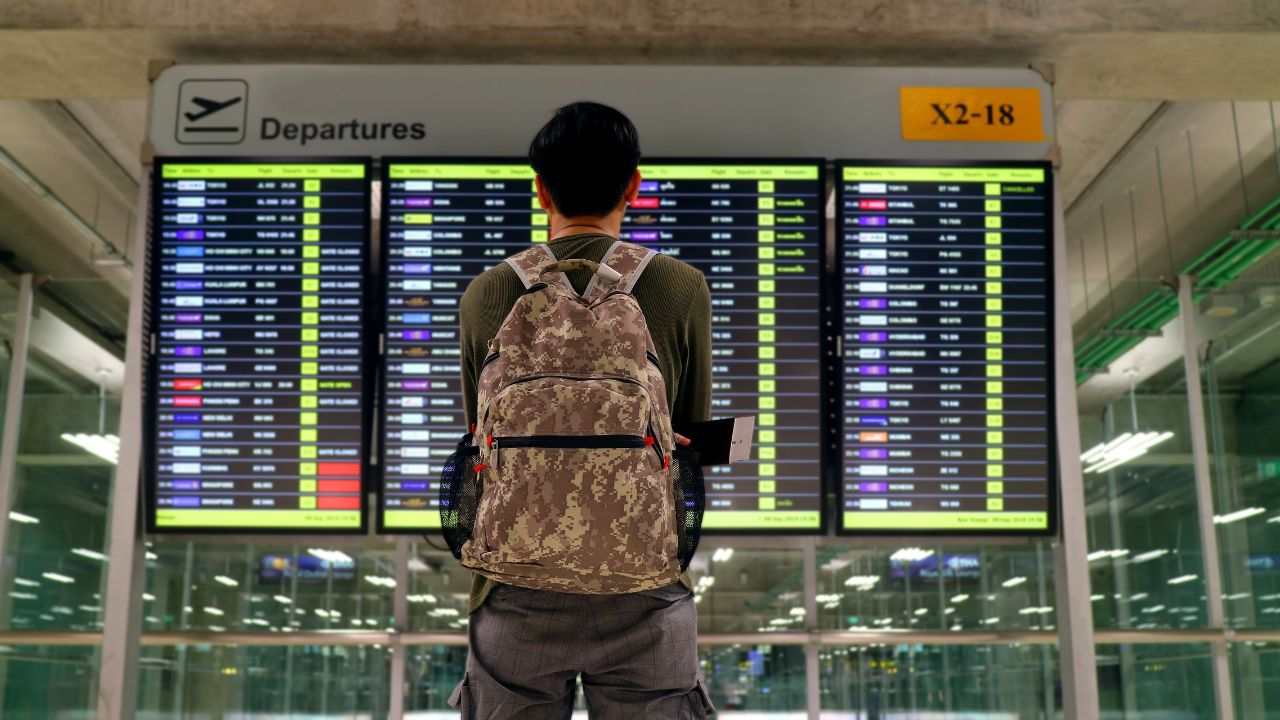 Young man with backpack looking at blurry flight information display screen at the airport