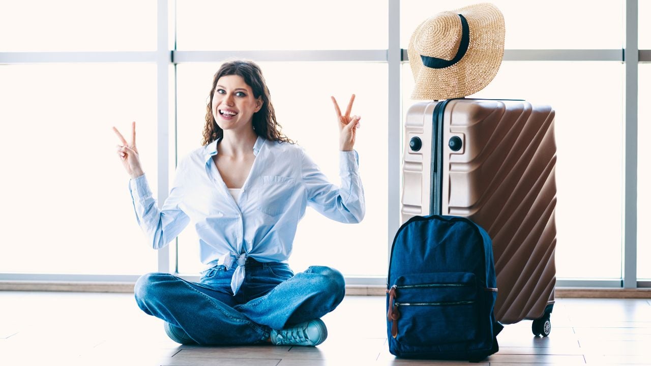 Passenger female traveler sitting at an airport terminal with luggage and backpack, depicting a carefree moment of journey preparation.