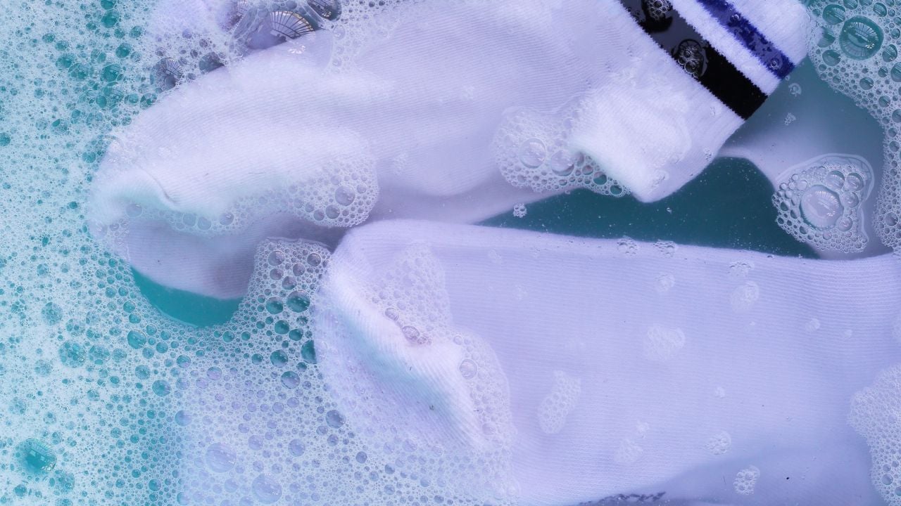 Dirty white socks soaked in water, dissolving detergent in blue basin.