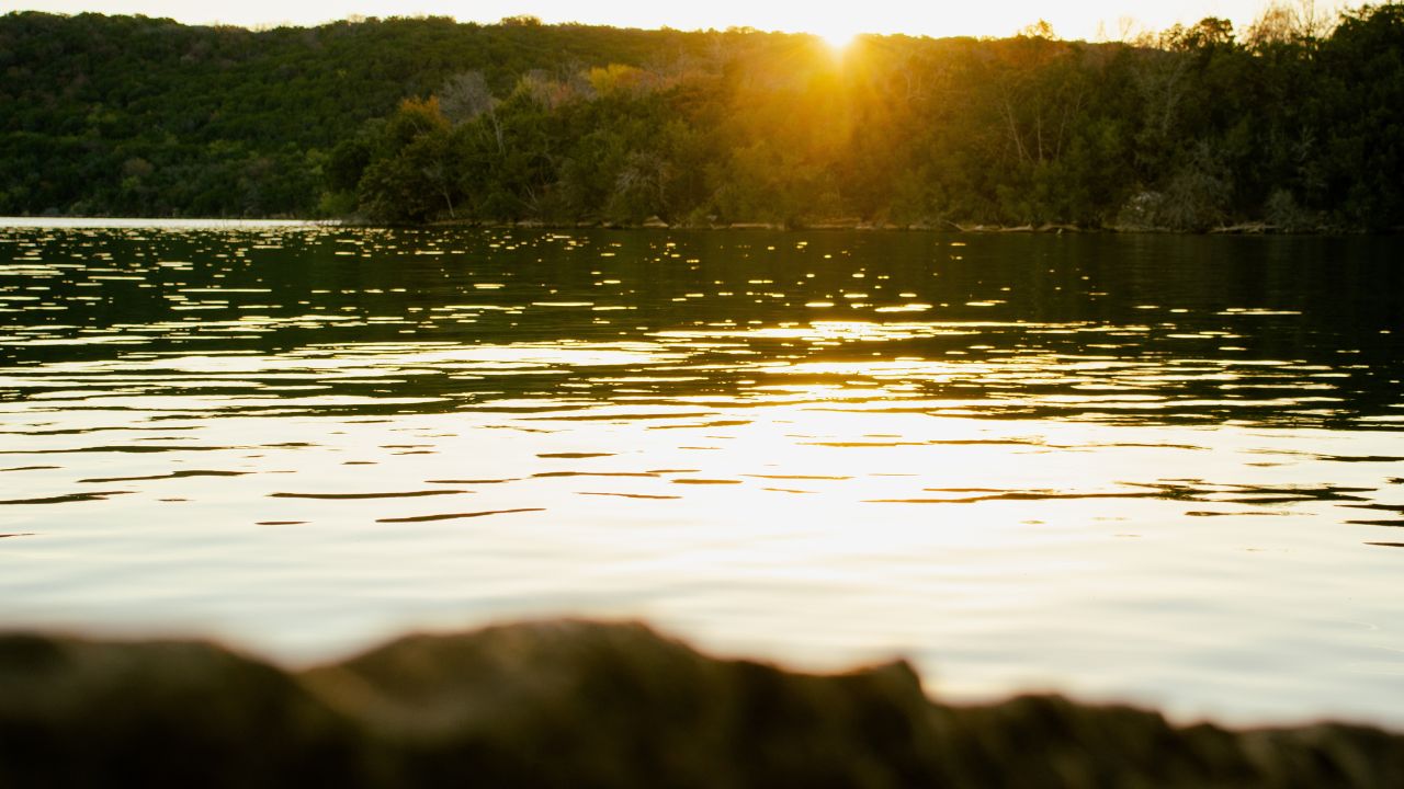 A scenic view of the Possum Kingdom lake reflecting the sun rays with green lush forests in the background