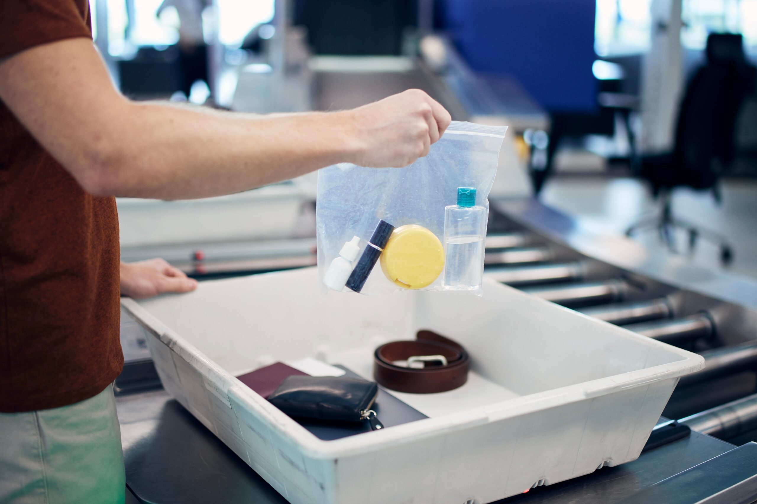 Airport security check before flight. Passenger holding plastic bag with liquids above container personal items.
