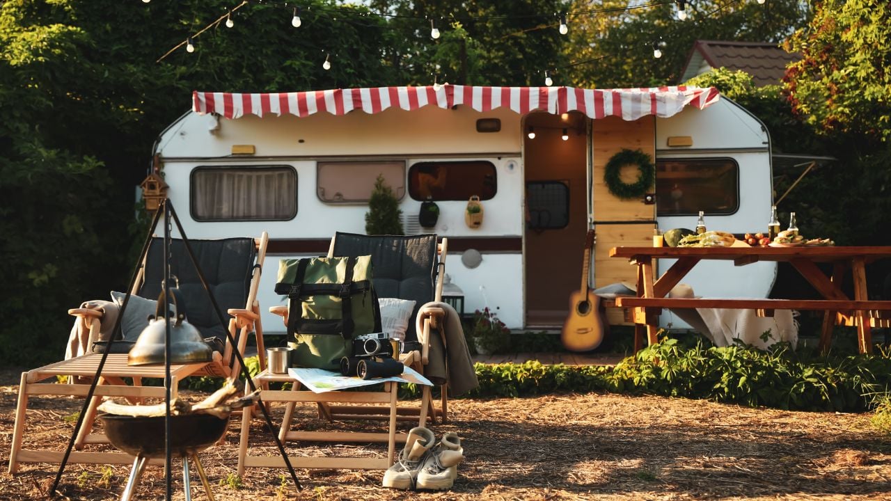 Deck chairs and travel accessories near modern trailer. Camping season